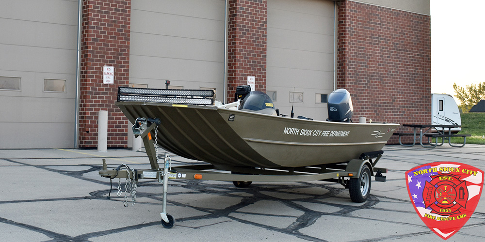 A North Sioux City Fire Department rescue boat on a trailer parked in front of a fire station.