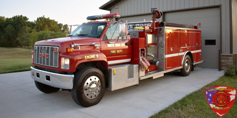 Red North Sioux City Fire Department GMC fire engine parked on a concrete driveway in front of a garage.