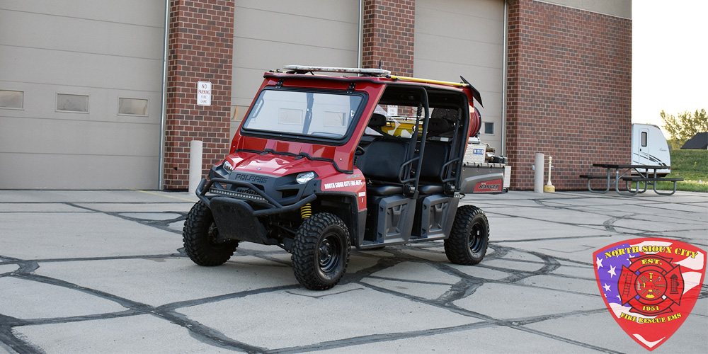 Red North Sioux City Fire Department utility vehicle parked outside a fire station, with the department’s emblem in the corner.