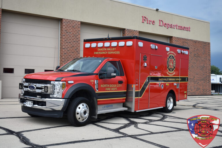 A red Dakota Valley Emergency Services ambulance parked in front of a fire station.