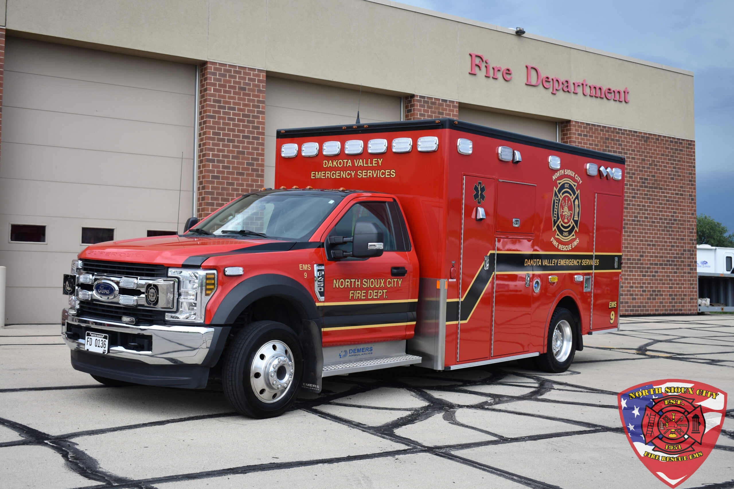 A red Dakota Valley Emergency Services ambulance parked in front of a fire station.