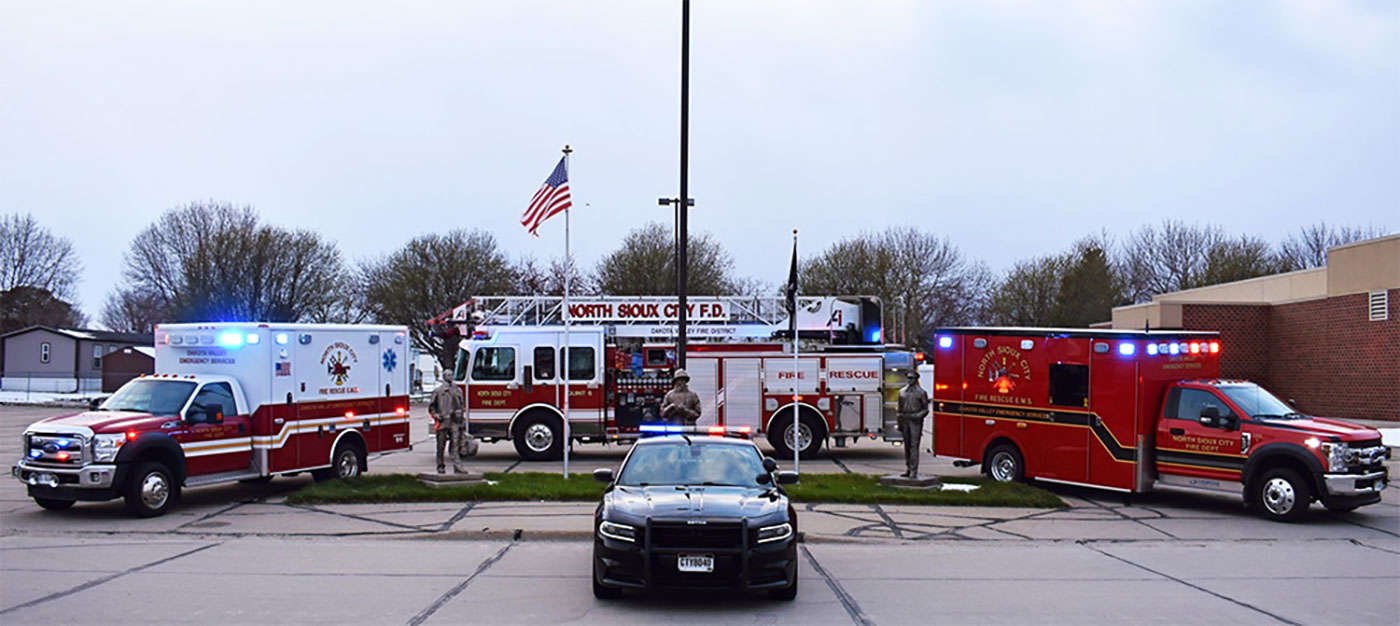 North Sioux City Fire and Rescue vehicles, including two ambulances and a fire engine, parked in a row with a police car in the foreground.