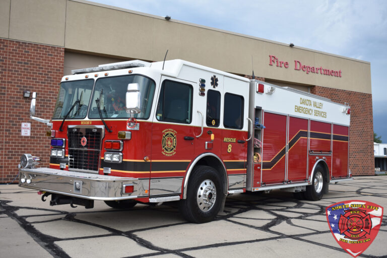 A red and white Dakota Valley Emergency Services fire rescue truck parked in front of a fire station.