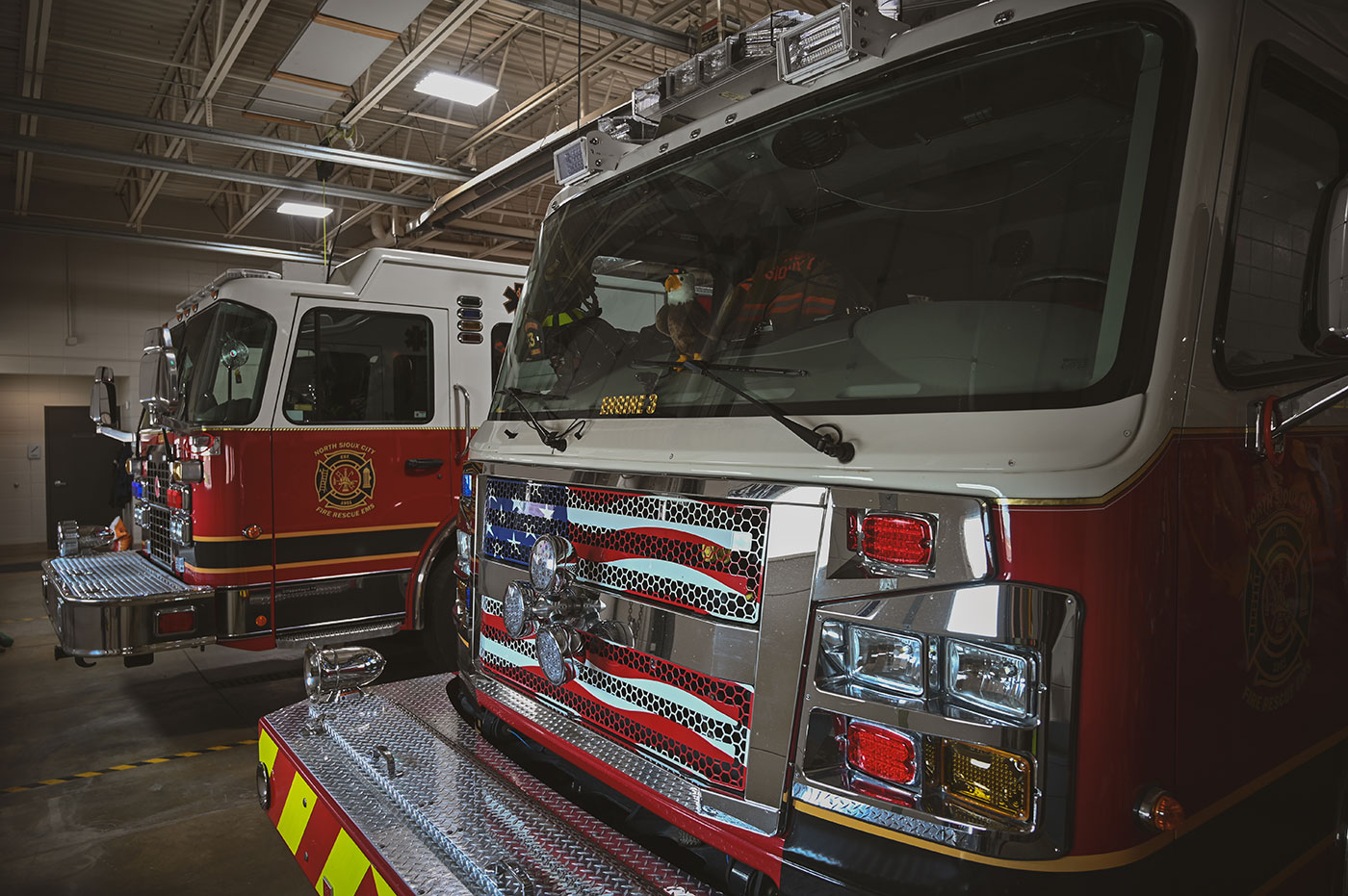 Two red and white North Sioux City fire trucks parked inside a fire station.
