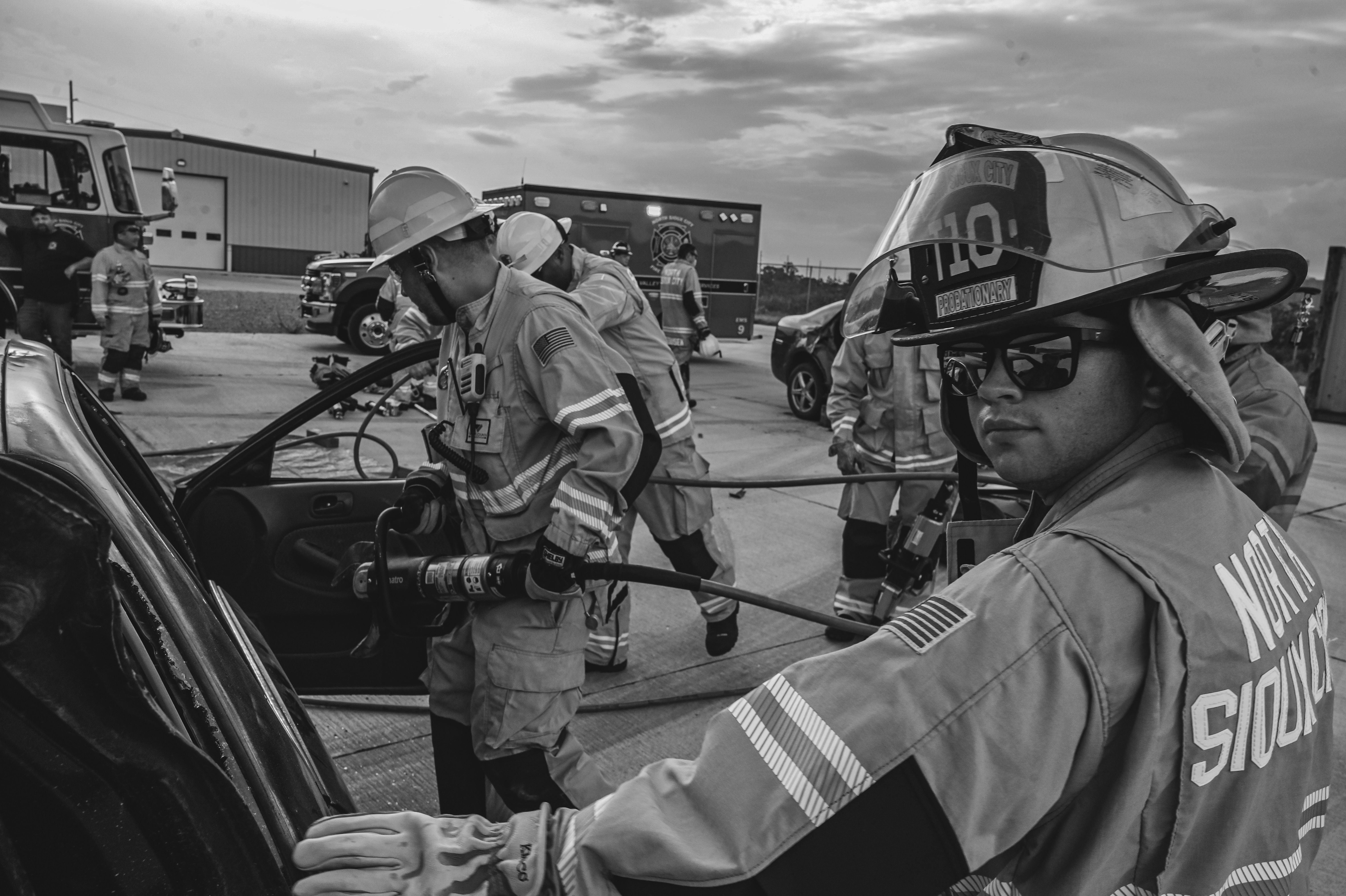 Firefighters in uniform and helmets use a rescue tool to cut into a car during a training exercise.