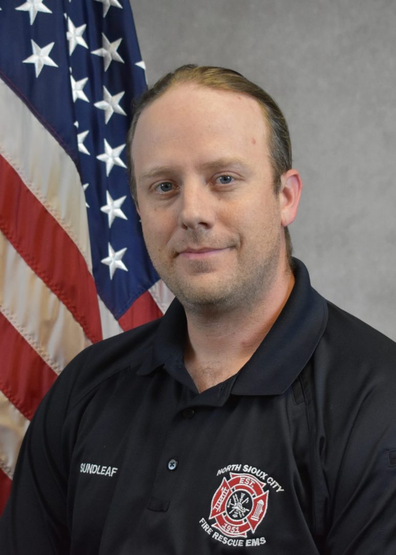 A North Sioux City Fire Rescue EMS official in a black uniform standing in front of an American flag.