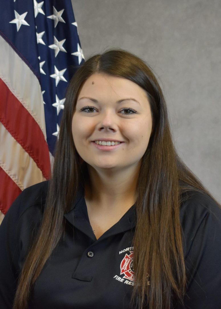 A woman in a black Northside Fire Rescue polo shirt posing in front of an American flag.