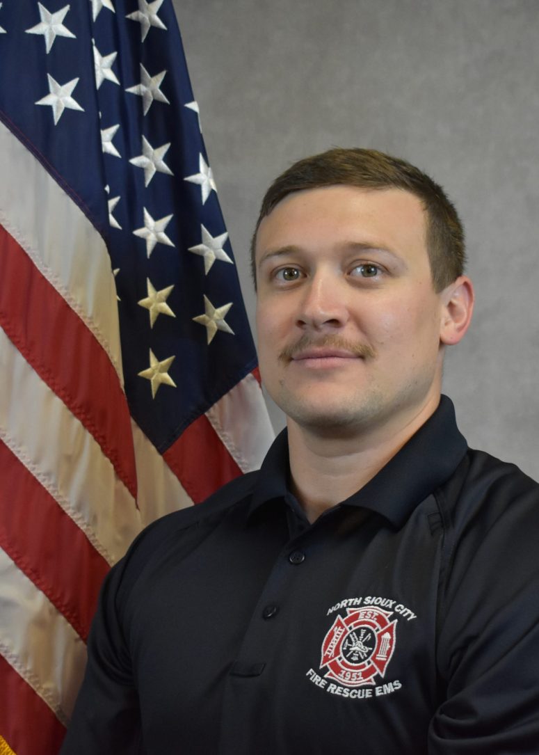A North Sioux City Fire Rescue EMS firefighter standing in front of an American flag.
