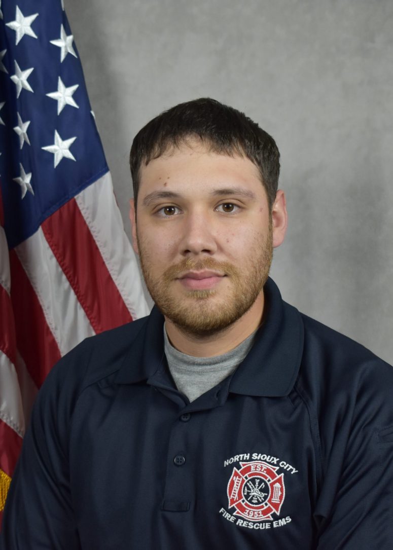 A North Sioux City Fire Rescue EMS personnel member standing in front of an American flag.